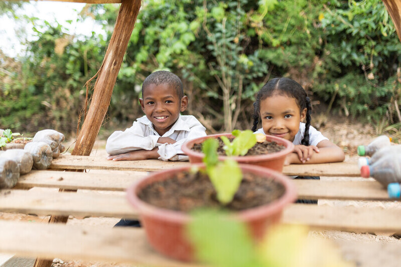 Photo of two children a school in Madagascar smiling at vegetables they are growing